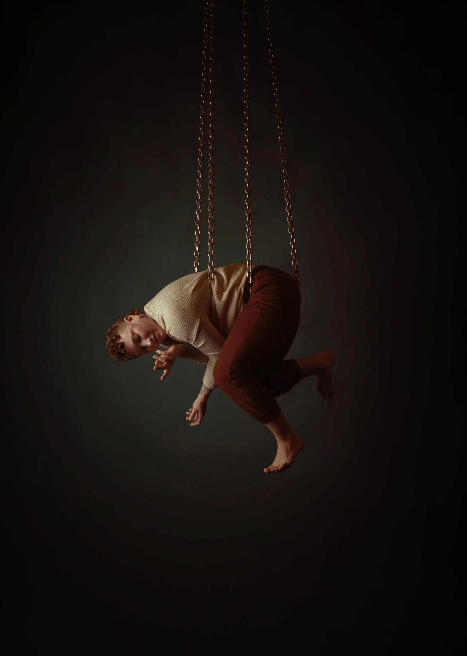 Alec hanging face-down in a tight cradled position on looped chains.